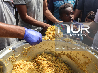 Palestinians receive cooked food rations as part of a volunteer initiative in a makeshift displacement camp in Deir Al-Balah, Gaza Strip, on...