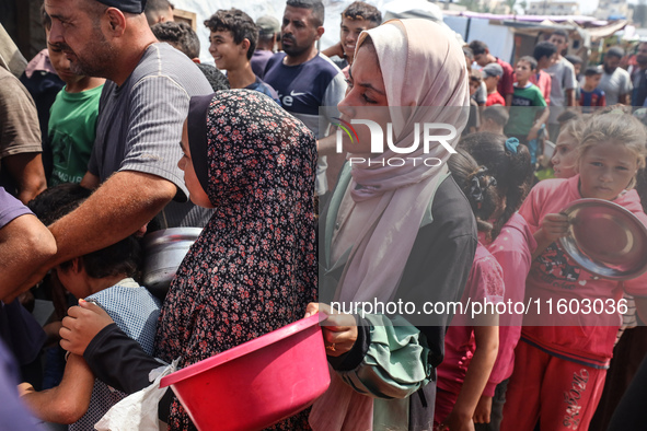 Palestinians receive cooked food rations as part of a volunteer initiative in a makeshift displacement camp in Deir Al-Balah, Gaza Strip, on...