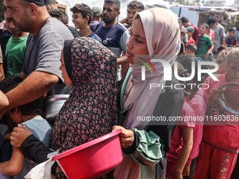 Palestinians receive cooked food rations as part of a volunteer initiative in a makeshift displacement camp in Deir Al-Balah, Gaza Strip, on...