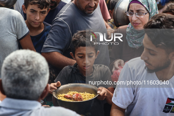 Palestinians receive cooked food rations as part of a volunteer initiative in a makeshift displacement camp in Deir Al-Balah, Gaza Strip, on...