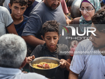 Palestinians receive cooked food rations as part of a volunteer initiative in a makeshift displacement camp in Deir Al-Balah, Gaza Strip, on...