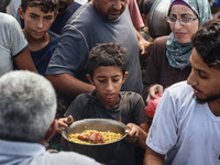 Palestinians receive cooked food rations as part of a volunteer initiative in a makeshift displacement camp in Deir Al-Balah, Gaza Strip, on...