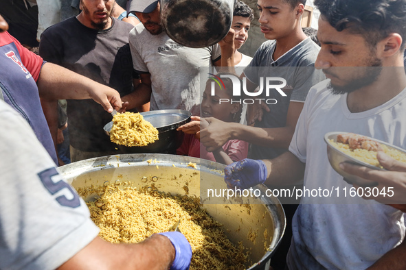 Palestinians receive cooked food rations as part of a volunteer initiative in a makeshift displacement camp in Deir Al-Balah, Gaza Strip, on...