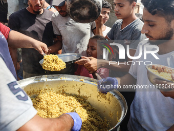 Palestinians receive cooked food rations as part of a volunteer initiative in a makeshift displacement camp in Deir Al-Balah, Gaza Strip, on...