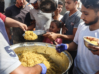 Palestinians receive cooked food rations as part of a volunteer initiative in a makeshift displacement camp in Deir Al-Balah, Gaza Strip, on...