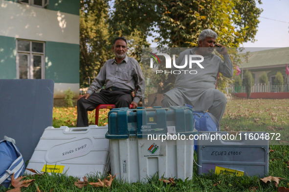 Polling officials sit beside electronic voting machines (EVM) at a distribution center on the eve of the second phase of voting during assem...