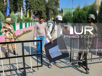 Indian security personnel stand guard as polling officials carry electronic voting machines (EVM) at a distribution center on the eve of the...