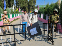 Indian security personnel stand guard as polling officials carry electronic voting machines (EVM) at a distribution center on the eve of the...