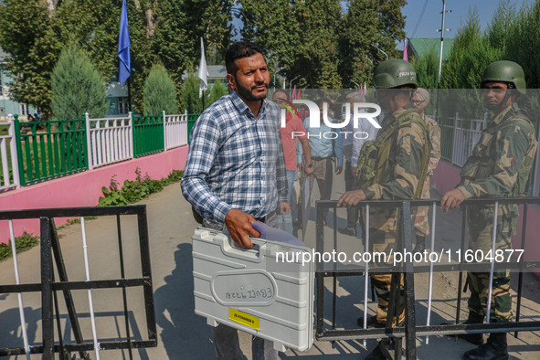 Indian security personnel stand guard as polling officials carry electronic voting machines (EVM) at a distribution center on the eve of the...