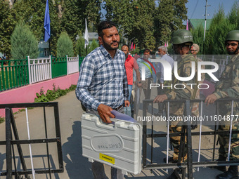 Indian security personnel stand guard as polling officials carry electronic voting machines (EVM) at a distribution center on the eve of the...