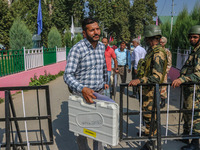 Indian security personnel stand guard as polling officials carry electronic voting machines (EVM) at a distribution center on the eve of the...