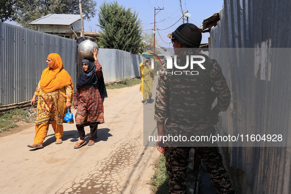 Women walk as paramilitary soldiers stand alert during an election campaign in Sopore, Jammu and Kashmir, India, on September 24, 2024 