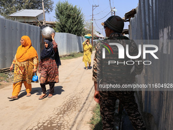 Women walk as paramilitary soldiers stand alert during an election campaign in Sopore, Jammu and Kashmir, India, on September 24, 2024 (