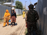 Women walk as paramilitary soldiers stand alert during an election campaign in Sopore, Jammu and Kashmir, India, on September 24, 2024 (