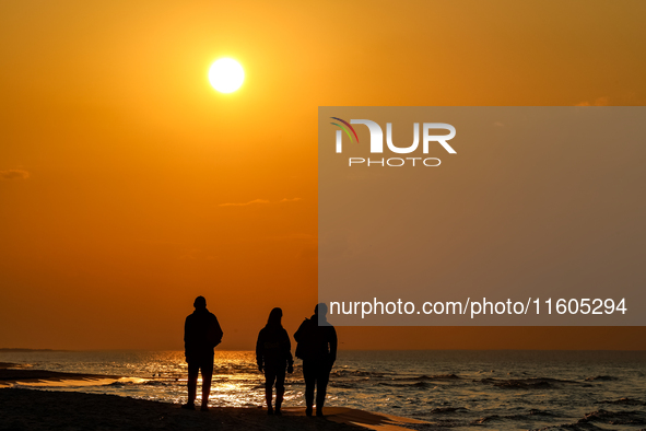 A tourist is seen walking on a beach in the evening against a setting sun on a sand beach by Baltic Sea near Leba, famous pomeranian tourist...