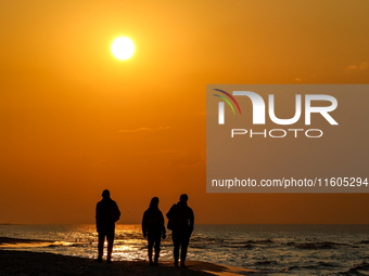 A tourist is seen walking on a beach in the evening against a setting sun on a sand beach by Baltic Sea near Leba, famous pomeranian tourist...