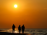 A tourist is seen walking on a beach in the evening against a setting sun on a sand beach by Baltic Sea near Leba, famous pomeranian tourist...