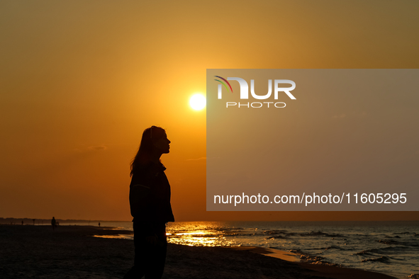 A tourist is seen walking on a beach in the evening against a setting sun on a sand beach by Baltic Sea near Leba, famous pomeranian tourist...