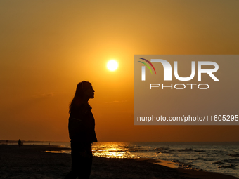 A tourist is seen walking on a beach in the evening against a setting sun on a sand beach by Baltic Sea near Leba, famous pomeranian tourist...