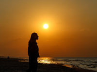 A tourist is seen walking on a beach in the evening against a setting sun on a sand beach by Baltic Sea near Leba, famous pomeranian tourist...