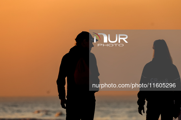 Tourists walk on a beach late in the afternoon as the sun sets on a sand beach by Baltic Sea near Leba, famous pomeranian tourist resort in...