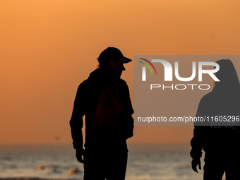 Tourists walk on a beach late in the afternoon as the sun sets on a sand beach by Baltic Sea near Leba, famous pomeranian tourist resort in...