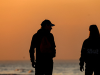 Tourists walk on a beach late in the afternoon as the sun sets on a sand beach by Baltic Sea near Leba, famous pomeranian tourist resort in...