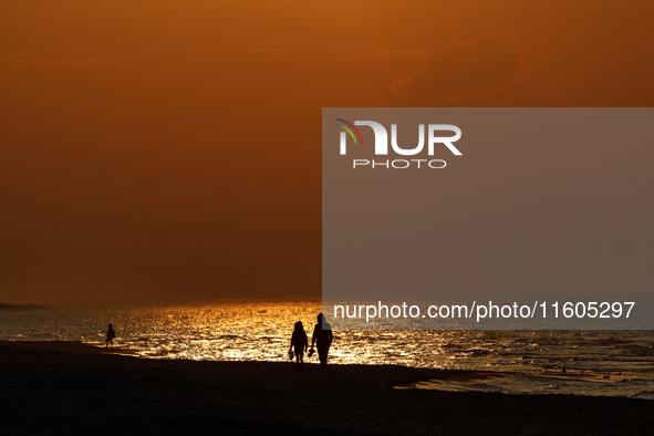 A couple walks on a beach  as the sun sets on a sand beach by Baltic Sea  near Leba, famous pomeranian tourist resort in northern Poland as...