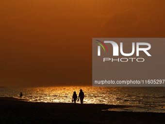 A couple walks on a beach  as the sun sets on a sand beach by Baltic Sea  near Leba, famous pomeranian tourist resort in northern Poland as...