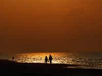 A couple walks on a beach  as the sun sets on a sand beach by Baltic Sea  near Leba, famous pomeranian tourist resort in northern Poland as...