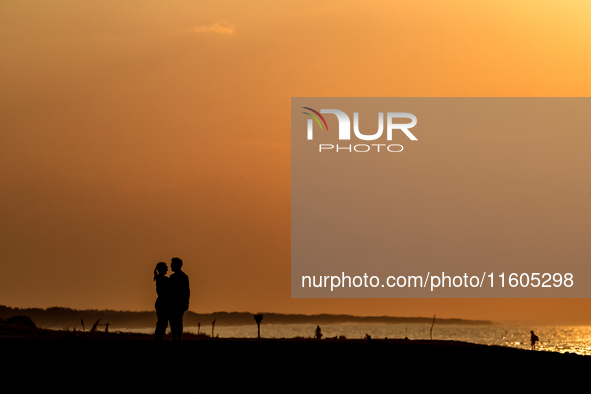 A couple holds on a beach  as the sun sets on a sand beach by Baltic Sea  near Leba, famous pomeranian tourist resort in northern Poland as...