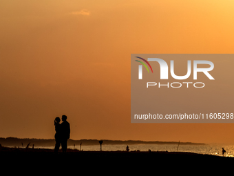 A couple holds on a beach  as the sun sets on a sand beach by Baltic Sea  near Leba, famous pomeranian tourist resort in northern Poland as...