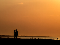 A couple holds on a beach  as the sun sets on a sand beach by Baltic Sea  near Leba, famous pomeranian tourist resort in northern Poland as...