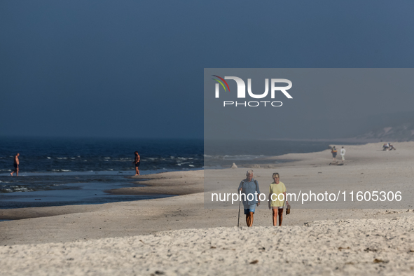 Tourists walk on a beach late in the afternoon as the sun sets on a sand beach by Baltic Sea near Leba, famous pomeranian tourist resort in...