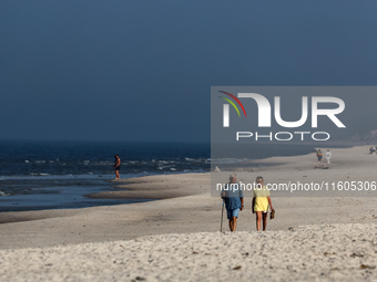 Tourists walk on a beach late in the afternoon as the sun sets on a sand beach by Baltic Sea near Leba, famous pomeranian tourist resort in...