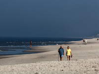 Tourists walk on a beach late in the afternoon as the sun sets on a sand beach by Baltic Sea near Leba, famous pomeranian tourist resort in...