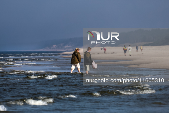 Tourists walk on a beach late in the afternoon as the sun sets on a sand beach by Baltic Sea near Leba, famous pomeranian tourist resort in...