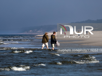 Tourists walk on a beach late in the afternoon as the sun sets on a sand beach by Baltic Sea near Leba, famous pomeranian tourist resort in...