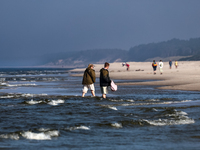 Tourists walk on a beach late in the afternoon as the sun sets on a sand beach by Baltic Sea near Leba, famous pomeranian tourist resort in...