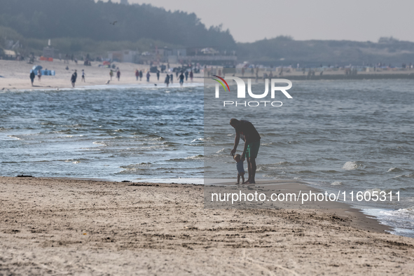 A father teaches a toddler to walk on a beach late in the afternoon as the sun sets on a sand beach by Baltic Sea near Leba, famous pomerani...