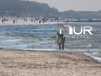 A father teaches a toddler to walk on a beach late in the afternoon as the sun sets on a sand beach by Baltic Sea near Leba, famous pomerani...