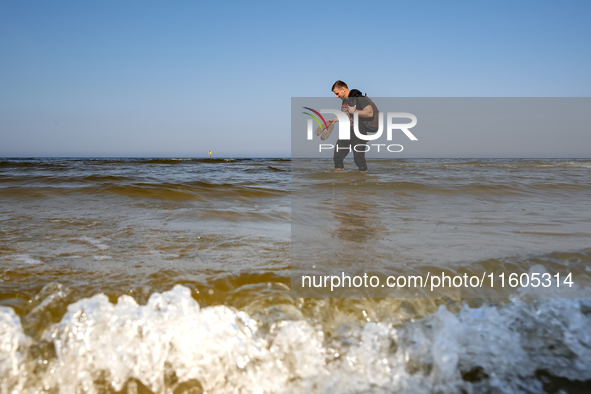 A tourist is seen walking in Baltic sea near a beach late in the afternoon as the sun sets on a sand beach near Leba, famous pomeranian tour...