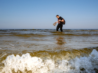 A tourist is seen walking in Baltic sea near a beach late in the afternoon as the sun sets on a sand beach near Leba, famous pomeranian tour...