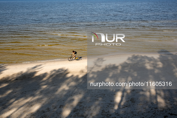 A tourist rides a bicycle on a beach late in the afternoon as the sun sets on a sand beach by Baltic Sea near Leba, famous pomeranian touris...