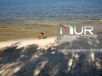 A tourist rides a bicycle on a beach late in the afternoon as the sun sets on a sand beach by Baltic Sea near Leba, famous pomeranian touris...