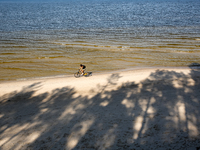 A tourist rides a bicycle on a beach late in the afternoon as the sun sets on a sand beach by Baltic Sea near Leba, famous pomeranian touris...