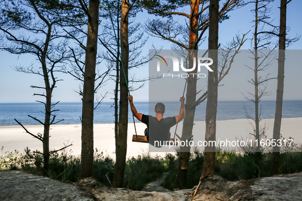 A tourist swings on a hand made swing on a beach late in the afternoon as the sun sets on a sand beach by Baltic Sea near Leba, famous pomer...