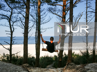 A tourist swings on a hand made swing on a beach late in the afternoon as the sun sets on a sand beach by Baltic Sea near Leba, famous pomer...