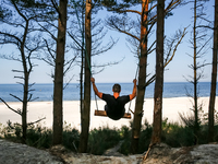 A tourist swings on a hand made swing on a beach late in the afternoon as the sun sets on a sand beach by Baltic Sea near Leba, famous pomer...