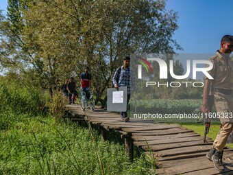 Polling officials, along with an Indian policeman, walk in the interiors of Dal Lake towards their designated polling station after collecti...